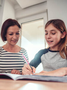 Mother helping daughter with math homework by the window at dining table