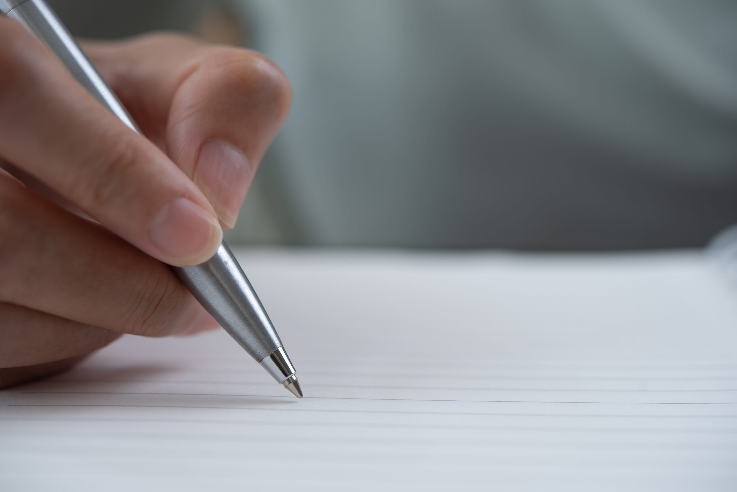 A close-up of a person's hand holding a silver pen, poised to write on a lined sheet of paper.