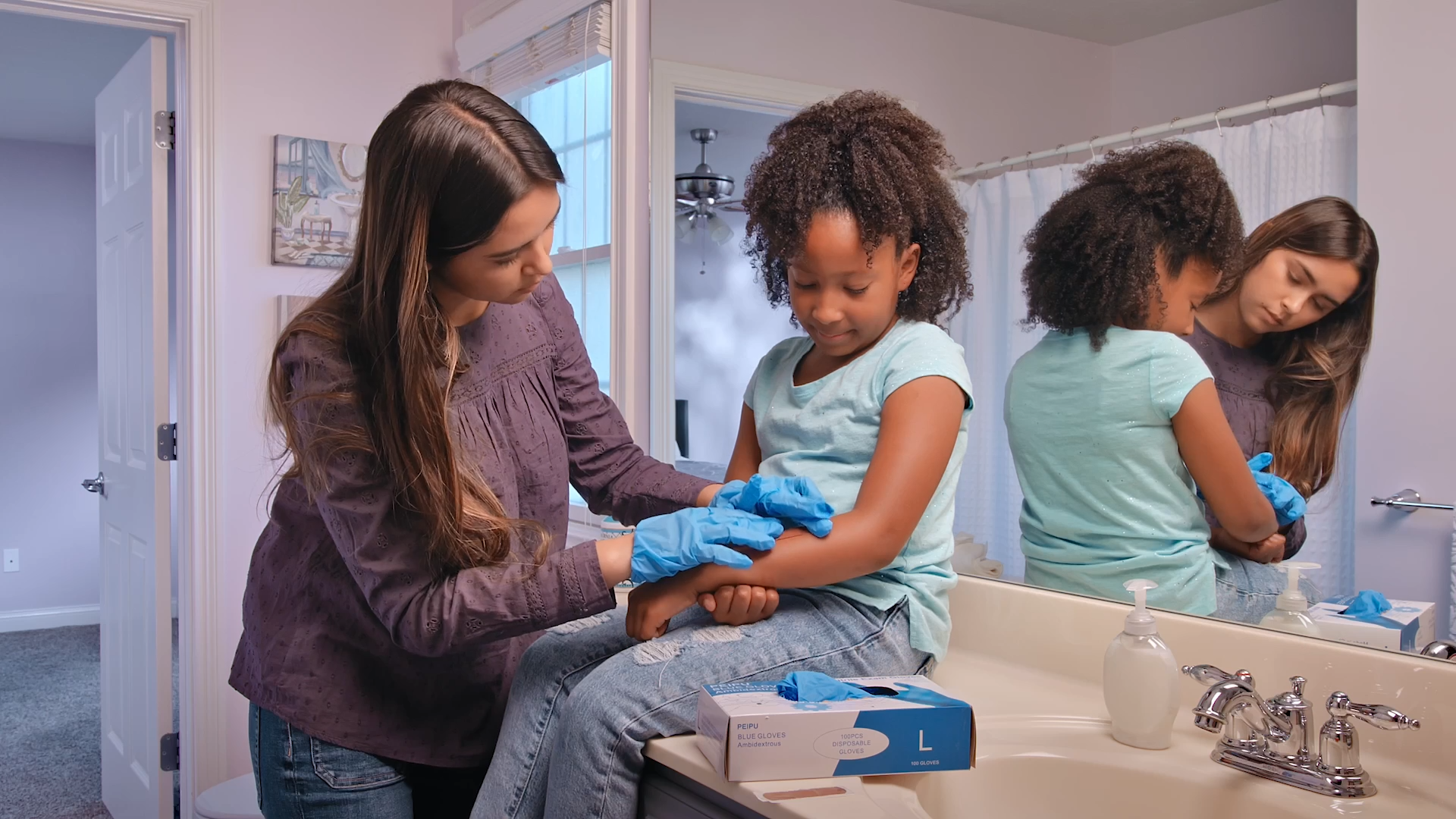 A young babysitter wearing blue gloves tends to a child's scraped arm in a bathroom setting, demonstrating first aid skills.